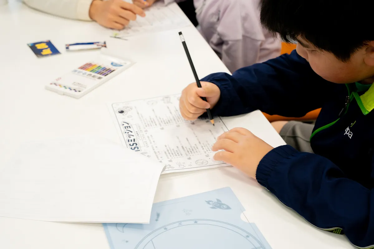宇宙飛行士見習いミッションのシートに書き込む子ども
