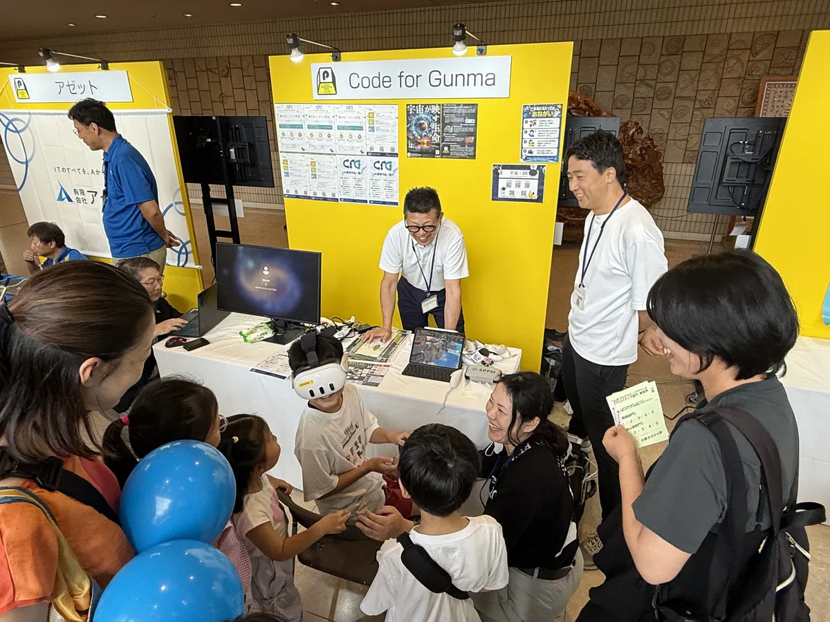 VRゴーグルでISSを体験する子どもと、順番を待つ家族
